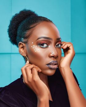 Stunning portrait of a stylish woman with creative makeup and hairstyle set against a vibrant blue backdrop.