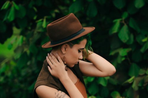 Free Profile of a stylish woman with tattoos and brown hat amidst greenery. Perfect for fashion and lifestyle themes. Stock Photo
