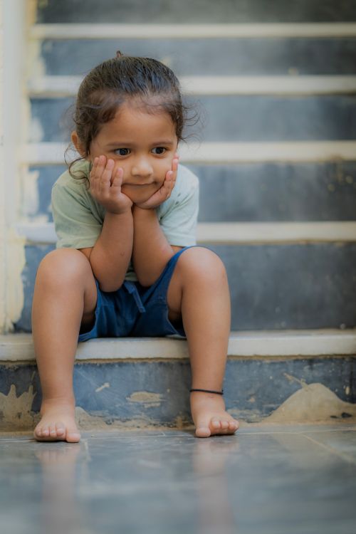 Free A cute child sitting with a thoughtful expression on indoor stairs, showcasing innocence. Stock Photo