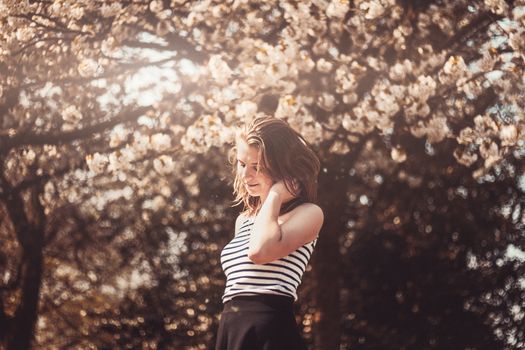 A young woman in a striped shirt enjoying the blooming cherry blossoms outdoors.