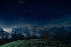 Beautiful starry night sky with a peaceful grassy hill and trees in the foreground.