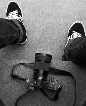 Feet in black sneakers next to a DSLR camera on a concrete floor in black and white