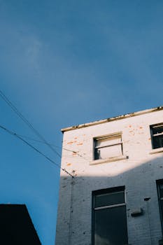 Low-angle shot of an urban building exterior with clear blue sky, showcasing its glass windows and shadowed facade.