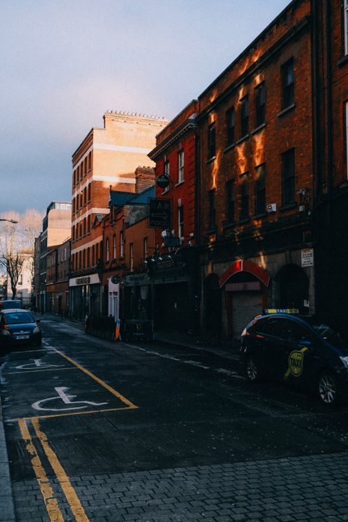 Free Sunlit street scene featuring historic red brick buildings and parked taxis. Stock Photo