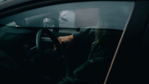 Free A person sitting inside a car with moody lighting, visible through the window. Stock Photo