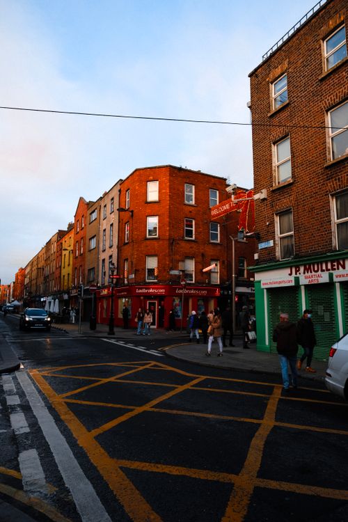 Free A bustling city street with pedestrians, cars, and urban buildings at sunset. Stock Photo