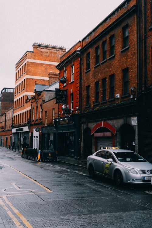 Free Urban street scene featuring red brick architecture and a parked taxi on a rainy day. Stock Photo