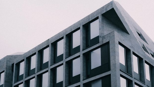 A sleek modern building with angular lines and glass windows captured in grayscale, showcasing urban architecture.