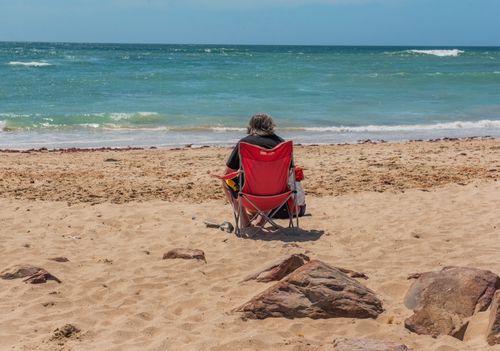 Free An adult sitting and relaxing by the ocean in Jeffreys Bay, capturing summer tranquility. Stock Photo