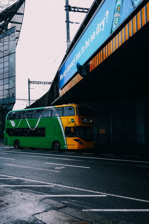 Free A green double-decker bus travels under a bridge in an urban setting with a poster above. Stock Photo