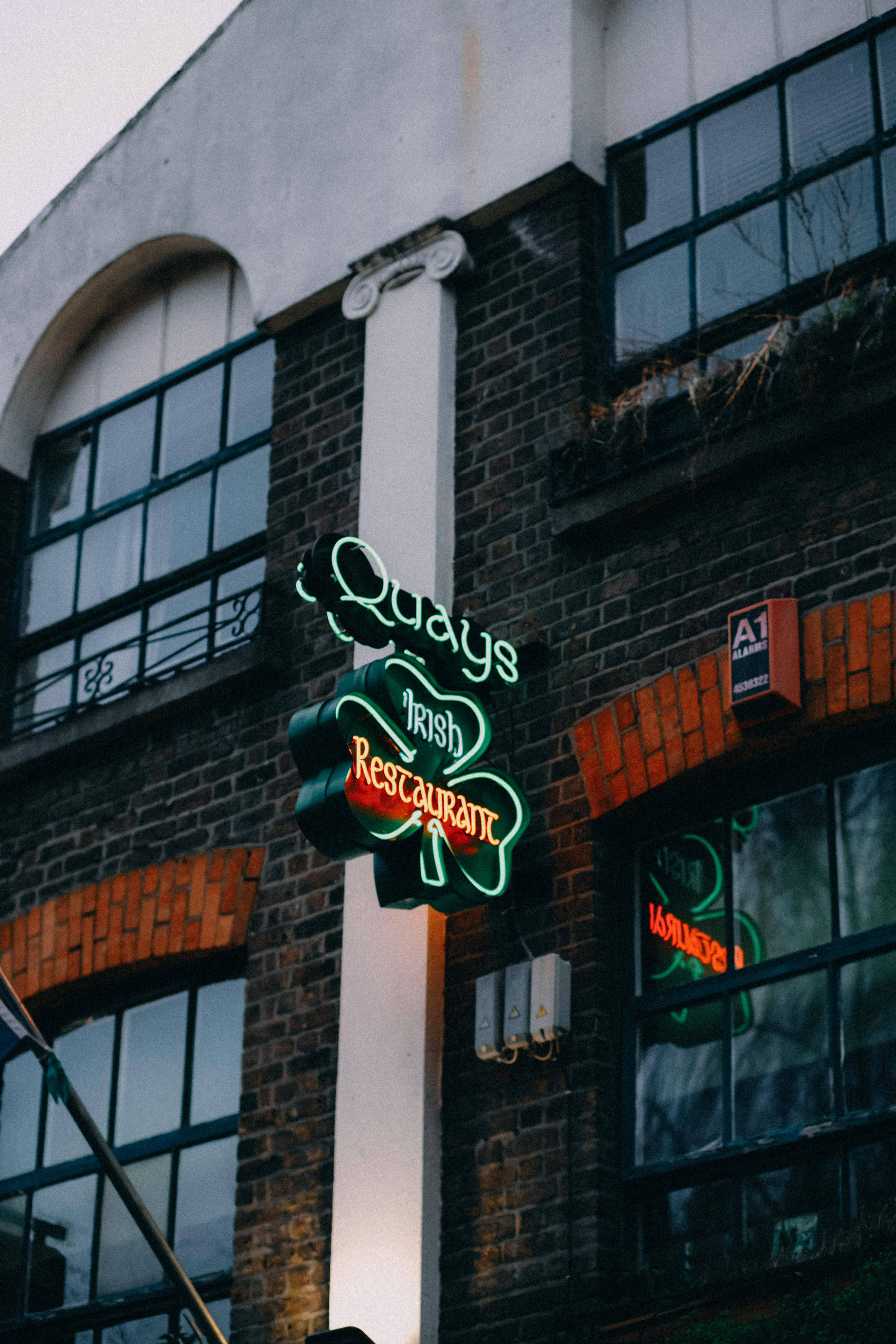 Captivating neon sign of Quays Irish pub with classic brick building facade, creating a vibrant urban atmosphere.