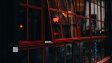 Slightly opened red-framed windows reflecting city lights at dusk, creating a vibrant contrast.