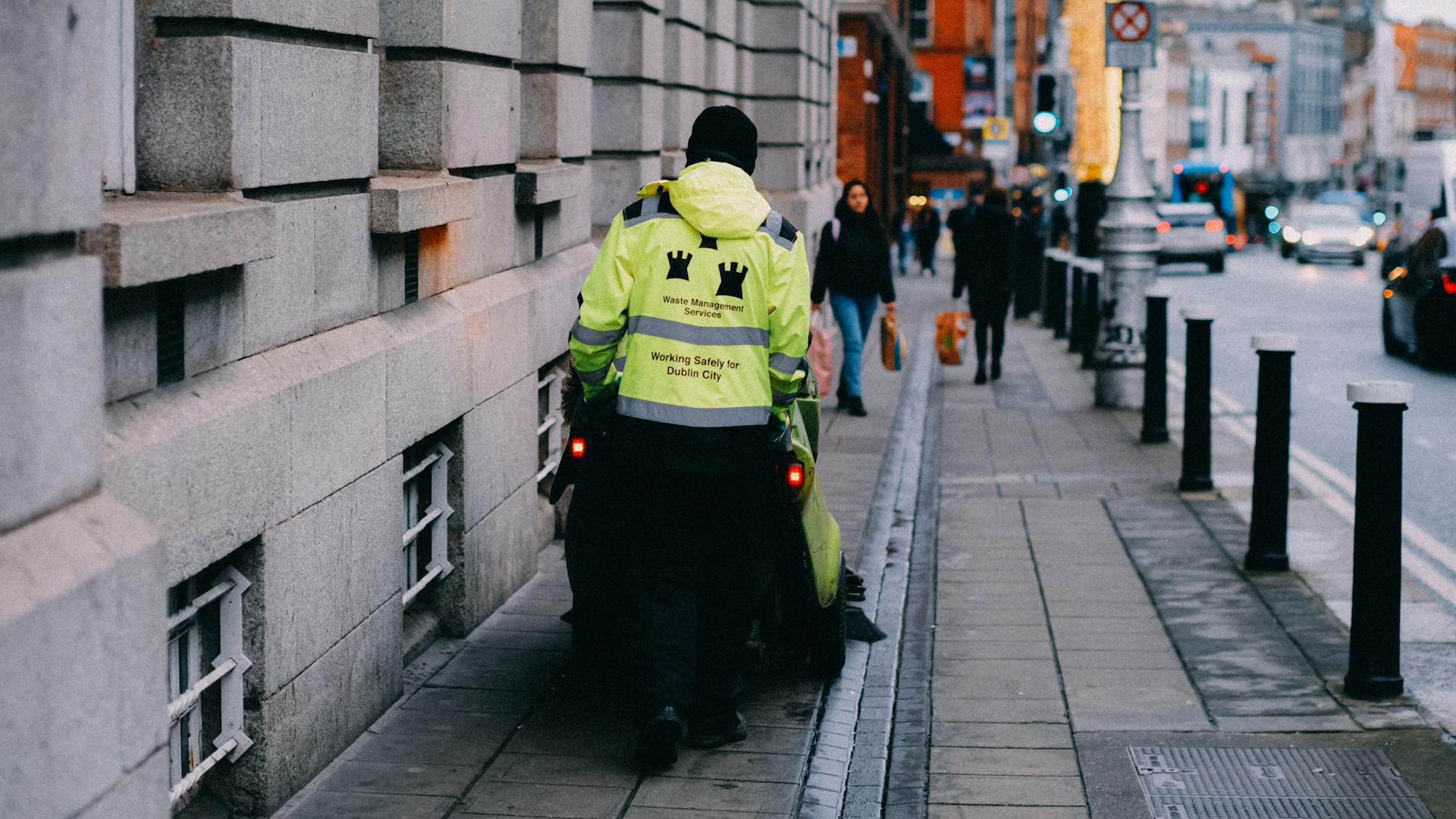 Street cleaner in Dublin wearing high-visibility gear on a city sidewalk.