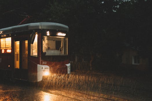 Tram moving at night through a rainy town with street lights illuminating the scene.