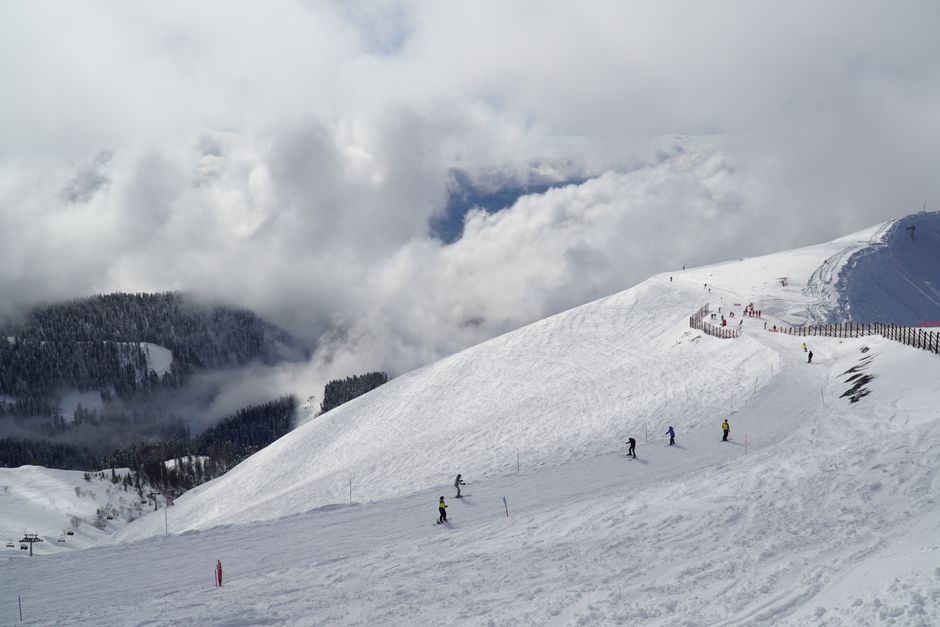 Skiers enjoy the snowy slopes of Adlerskiy amidst stunning mountain views and cloud formations.