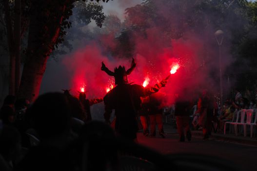 Silhouetted performers with flares create a dramatic scene at a nighttime festival parade.