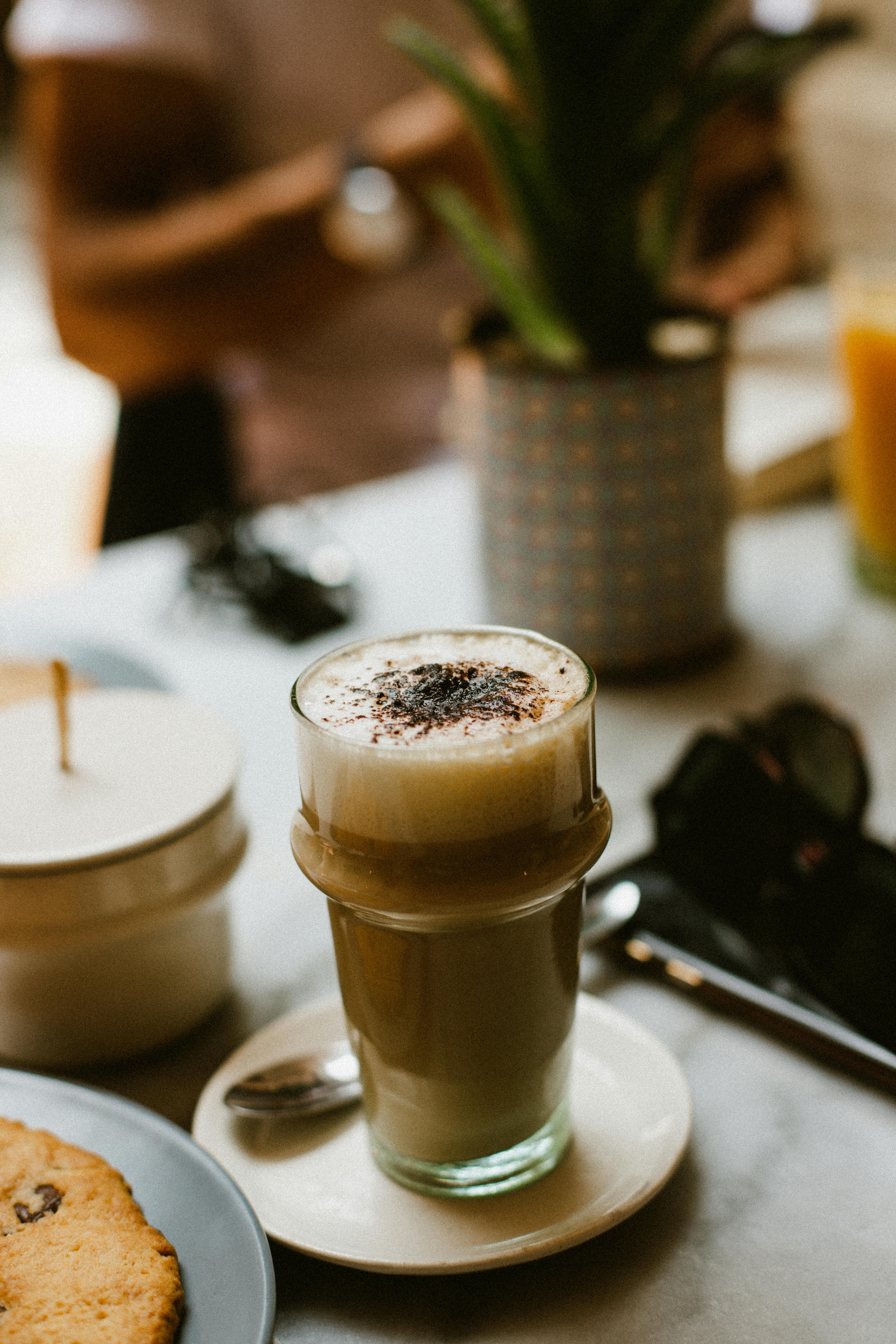 A creamy cafe latte with foam in a glass on a marble table setting in a cozy cafe.