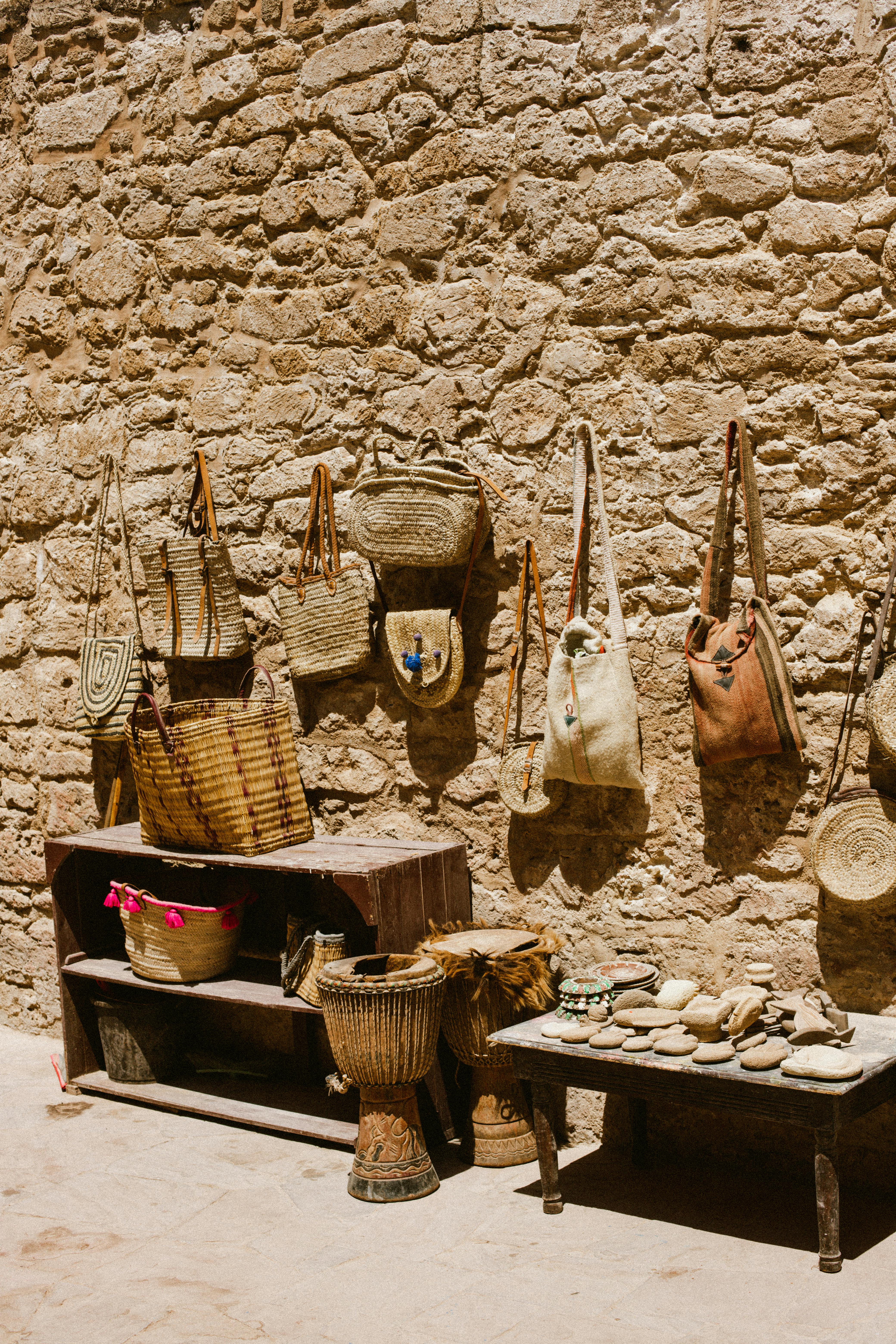 A display of handmade woven bags hanging on a rustic stone wall at an outdoor market.