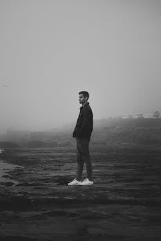 A solitary man stands on a foggy beach in Rabat, Morocco, with a moody atmosphere.
