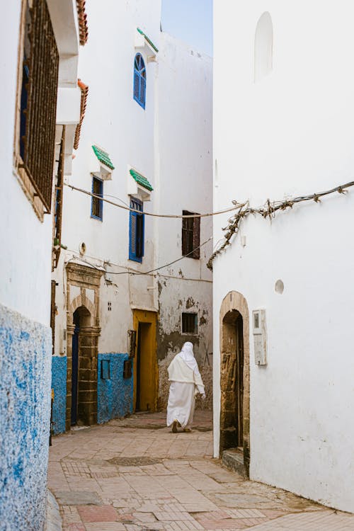 Free Person Walking on Narrow Street Between White Buildings  Stock Photo