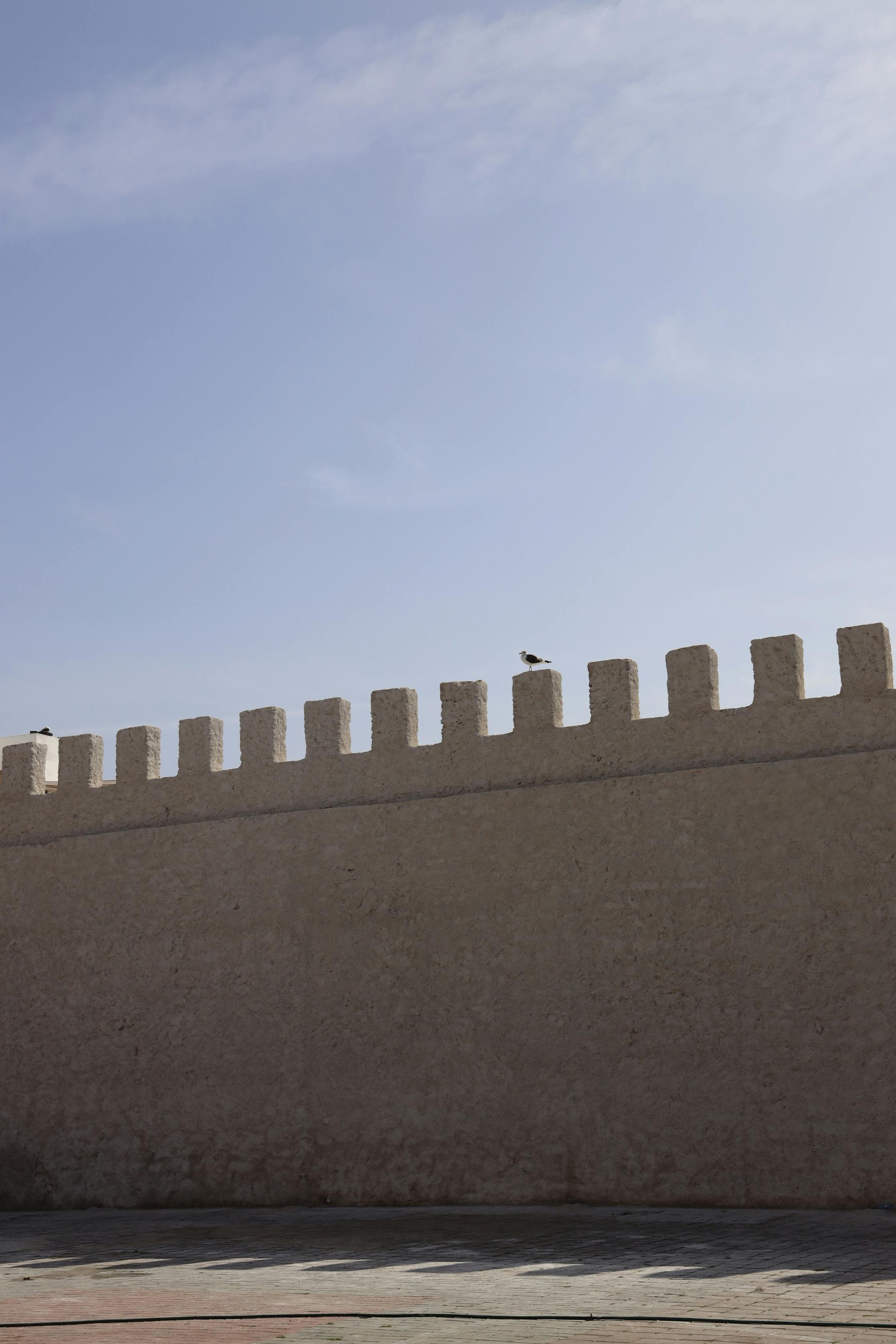 Free A historic stone wall under a clear blue sky provides a minimalist architectural view. Stock Photo