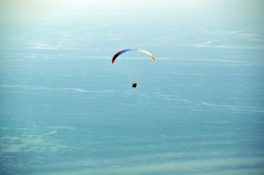 A solitary paraglider gracefully glides over the calm blue ocean, capturing the essence of freedom and adventure.