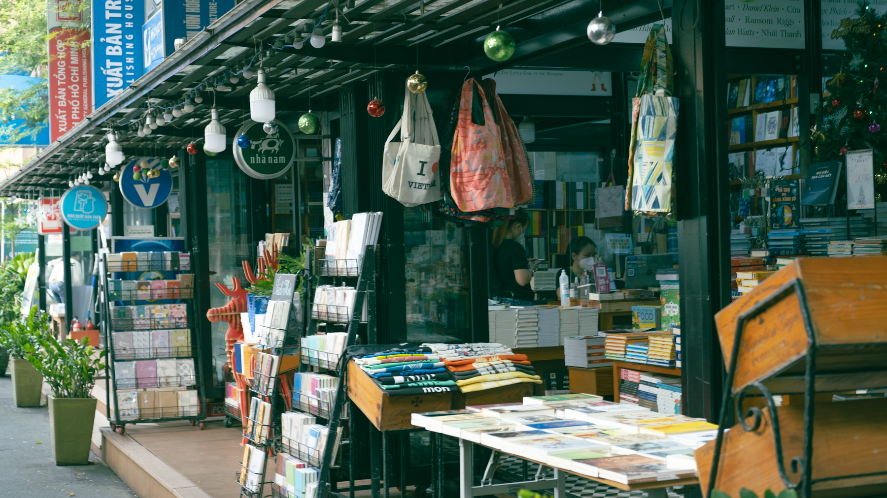 Explore a bustling street market bookshop in Vietnam, showcasing books and bags in a colorful outdoor setting.