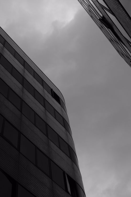 Free A dramatic black and white photo of modern buildings reaching into the cloudy sky. Stock Photo