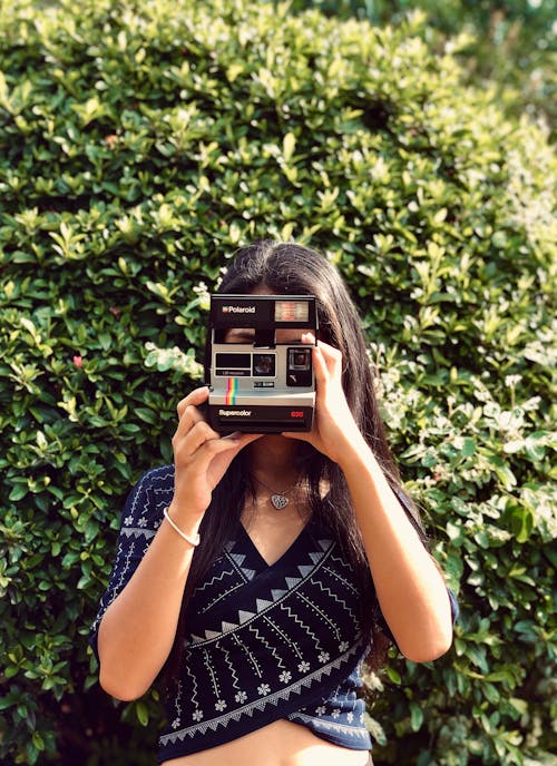 Woman Standing near the Green Plants Holding a Polaroid 635 Supercolor Instant Camera