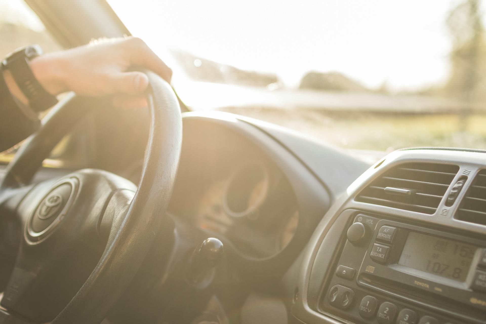 Interior view of a car being driven, highlighting the steering wheel in a sunlit cabin.