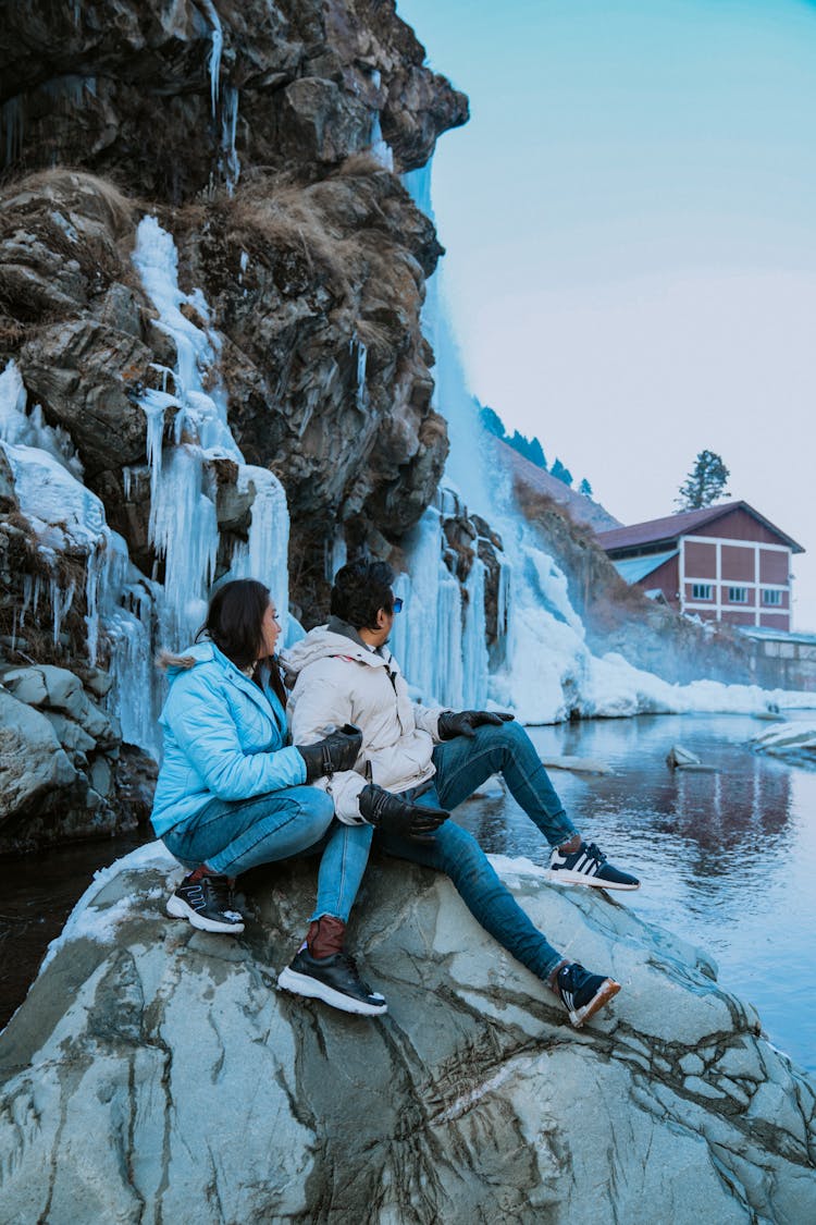 Couple Sitting On Rock By Frozen Waterfalls