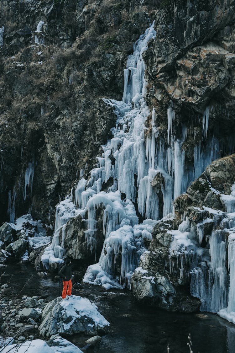 Man On Rock Near Frozen Waterfall