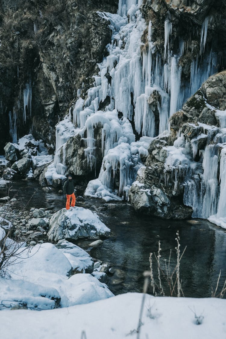 Man On Rock Near Winter Frozen Waterfall