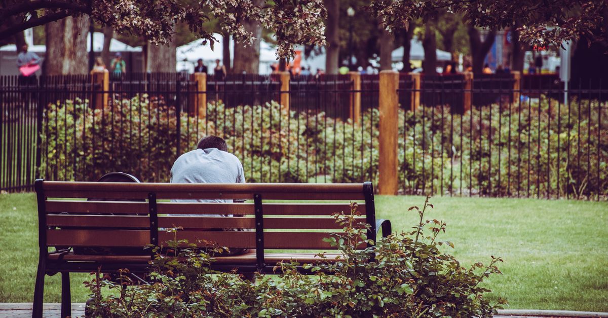 A person sitting alone on a park bench at sunrise, looking contemplative