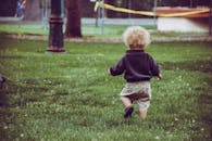 一个卷发幼儿在公园草地上快乐地走着，捕捉到了童年的纯真