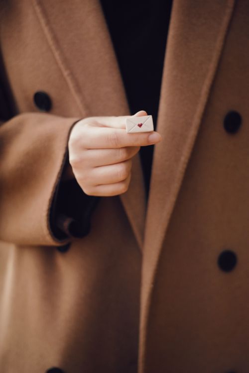 Free A hand in a coat holding a miniature love letter, symbolizing affection. Stock Photo