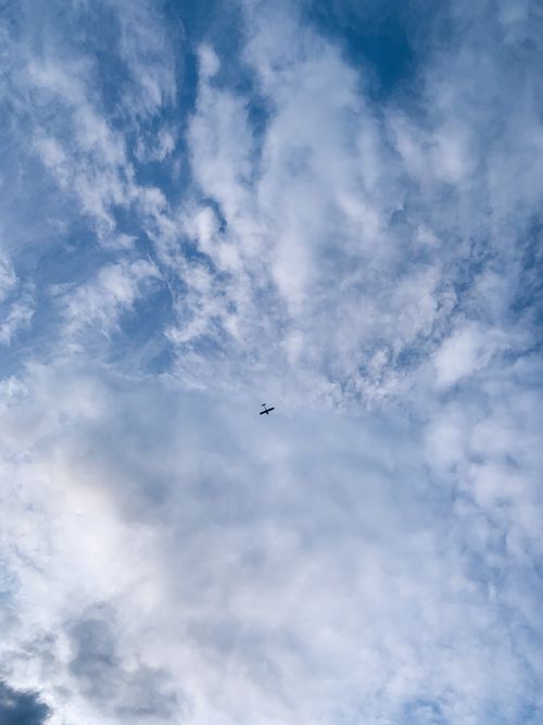 Free A distant airplane soars through a vast cloud-filled sky, showcasing a serene and peaceful atmosphere. Stock Photo