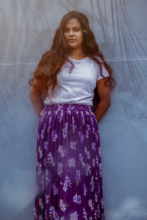 Woman Leaning Against a Wall in White Shirt and Purple Floral Long Skirt