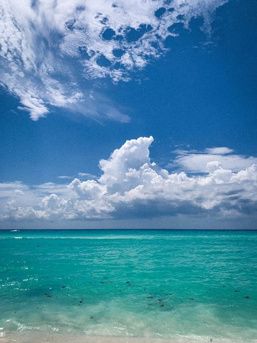 Free A breathtaking view of a tropical beach with vibrant waters and dramatic clouds under a clear sky. Stock Photo