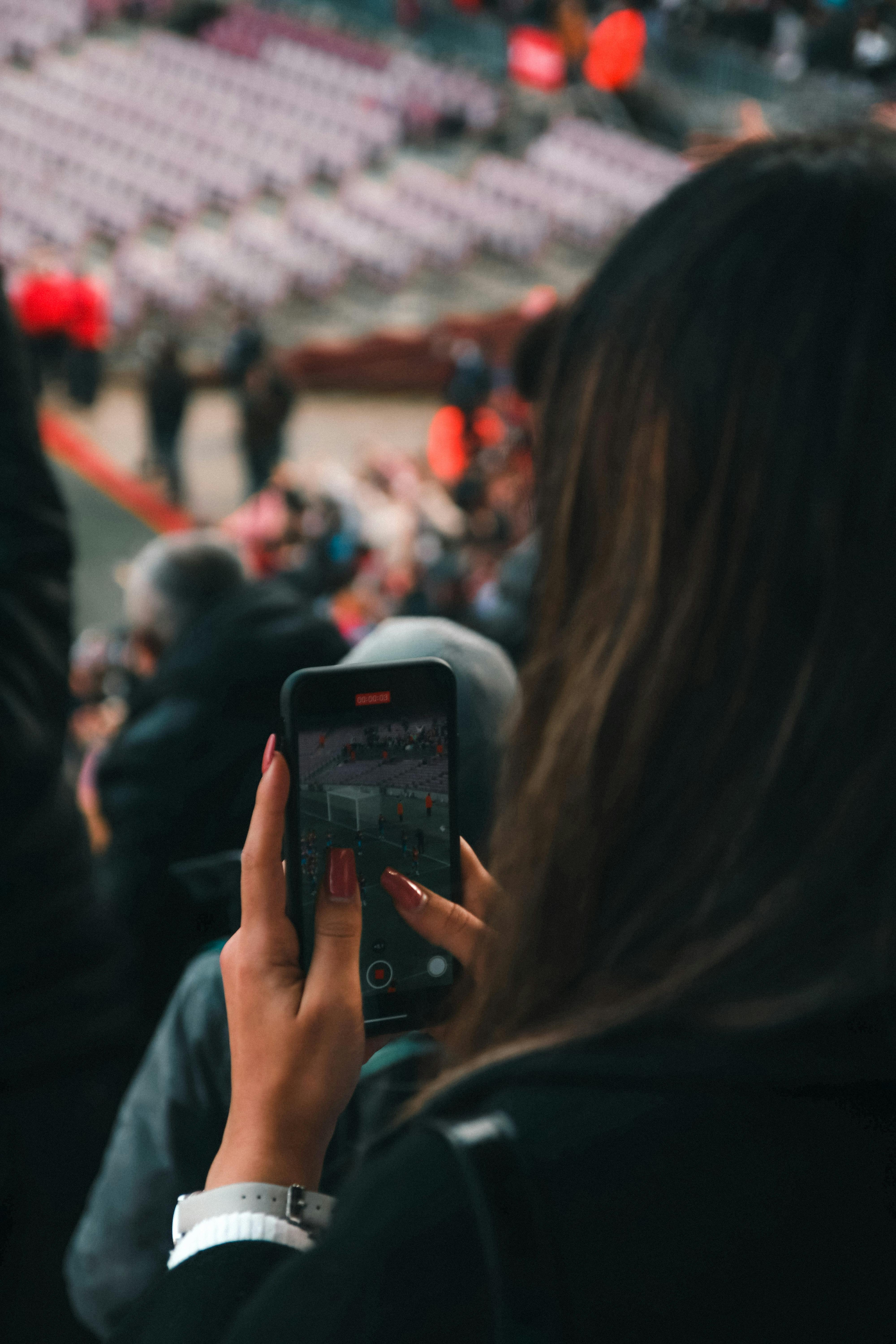 Woman photographing event with smartphone from the crowd.