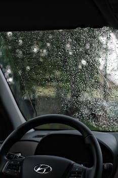 View from inside a car showing rain-soaked windshield and blurred outdoor scene.