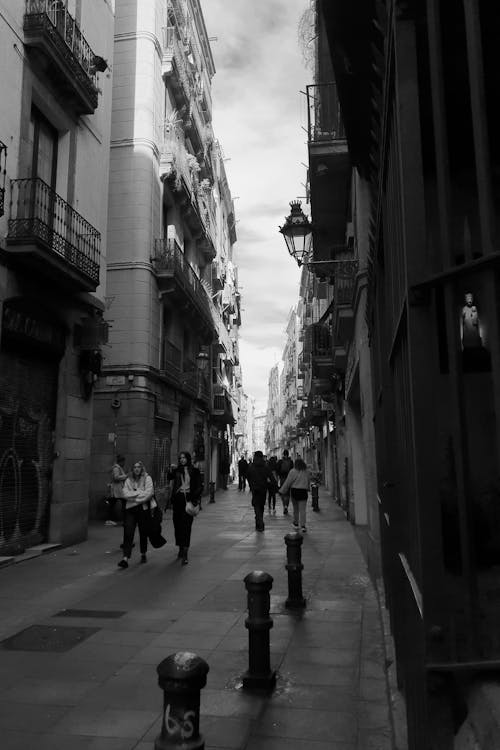 Black and White Photograph of People Walking on a Narrow City Street