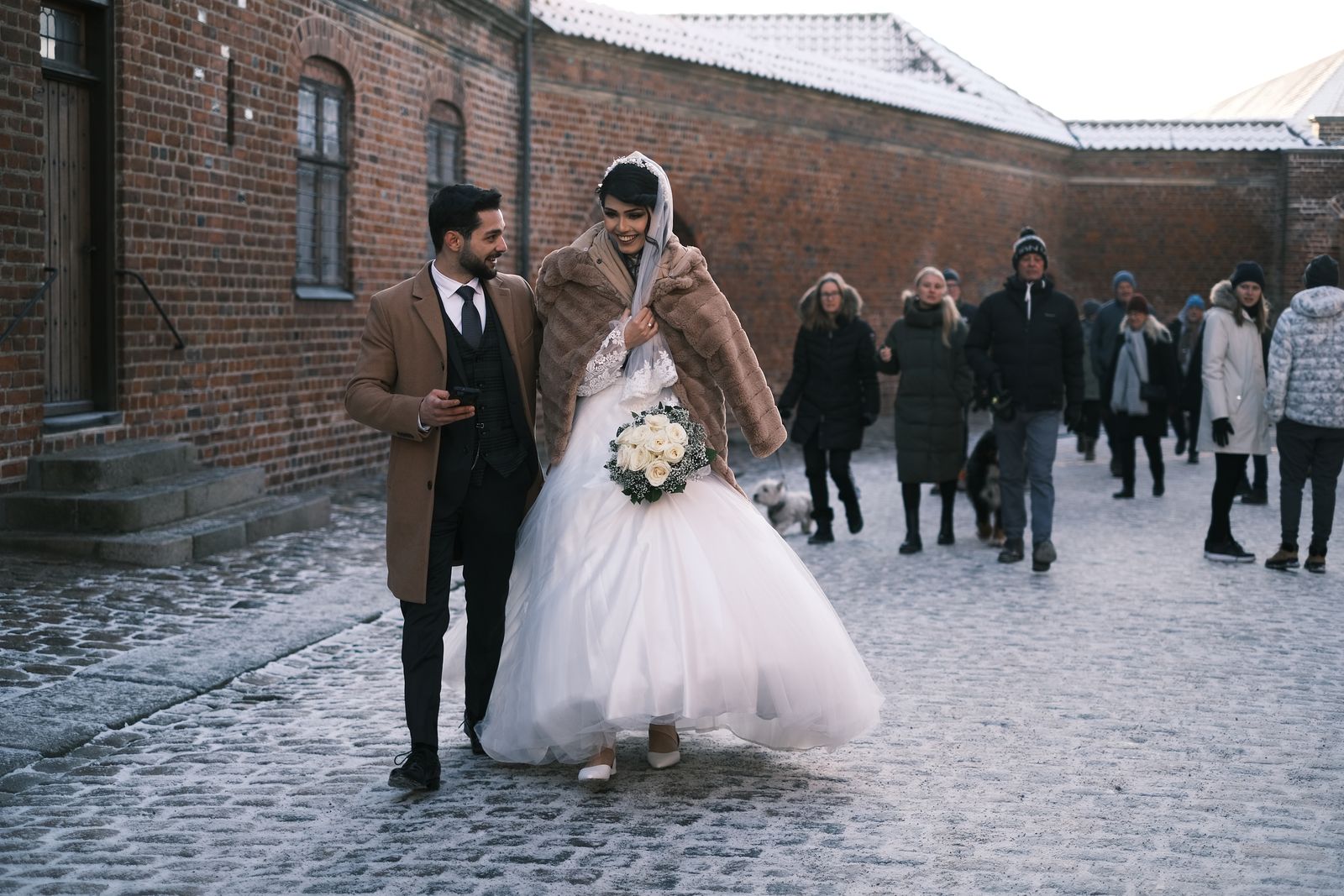 Wedding party walking down a snowy street surrounded by guests