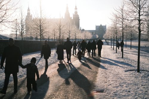 Free People walking on a snowy path by Frederiksborg Castle, Denmark in winter sunlight. Stock Photo