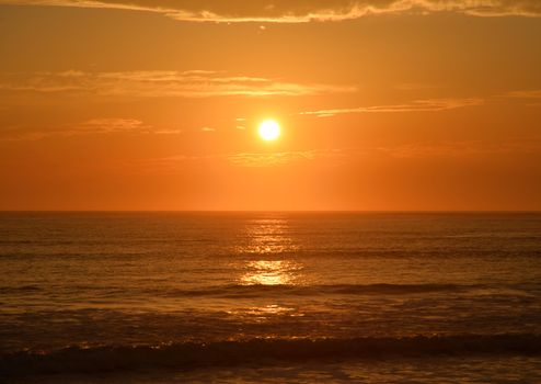 Stunning sunset over the ocean with a vibrant orange sky reflecting on calm waters.