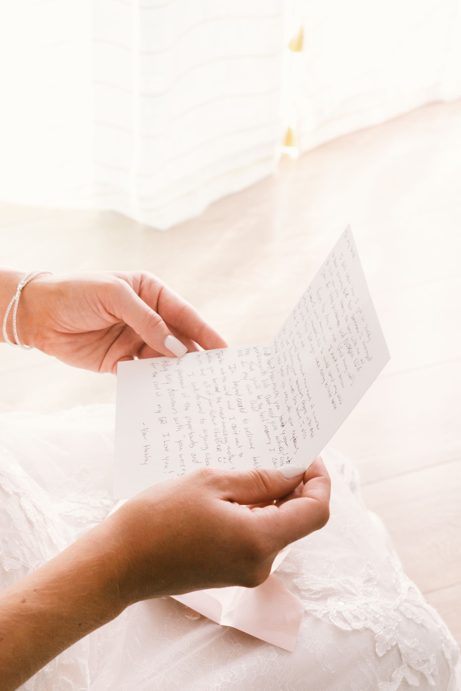 Hands holding a handwritten letter above pale bed linen