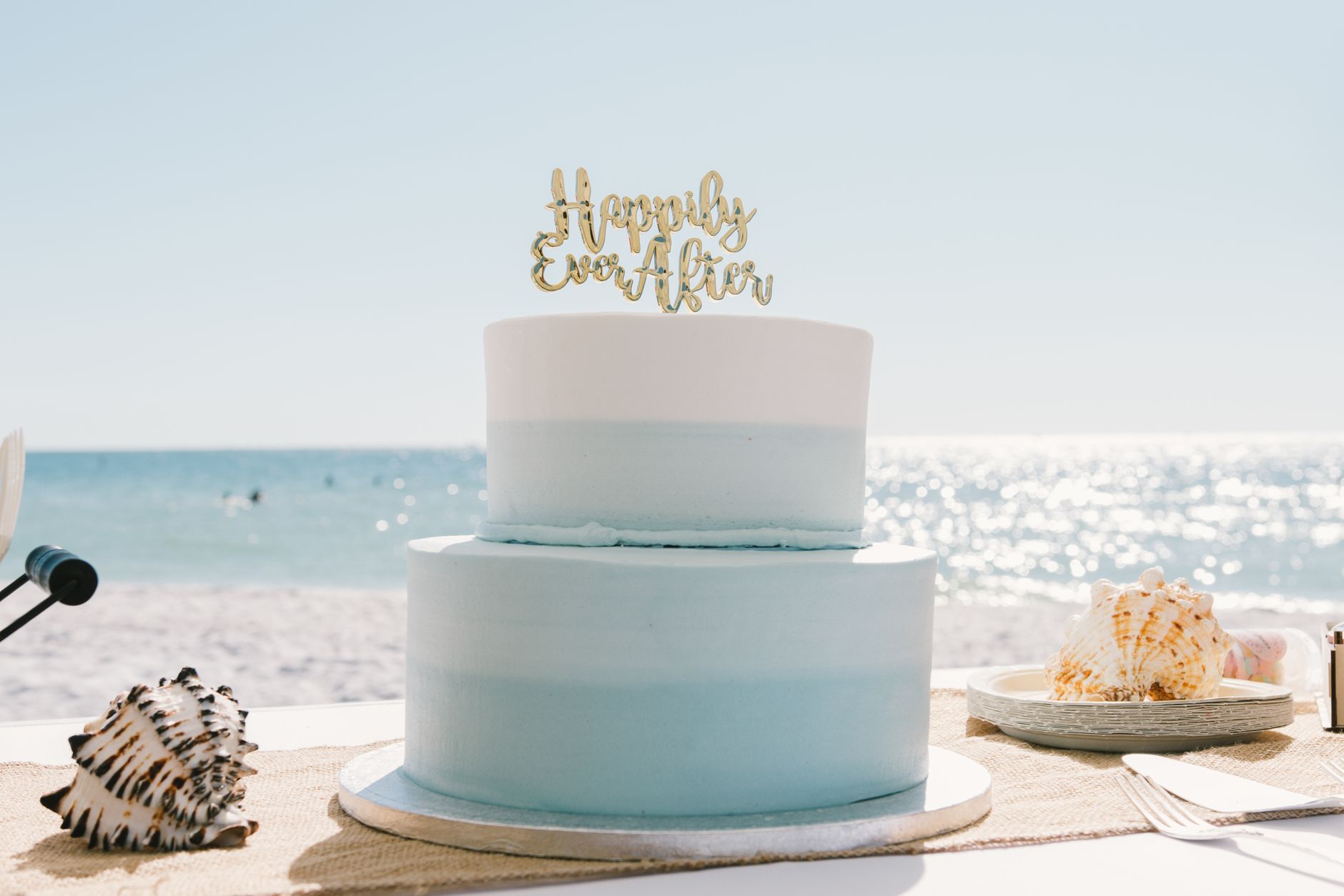 Beautiful beach wedding cake with seashells under a sunny sky, perfect for coastal weddings.