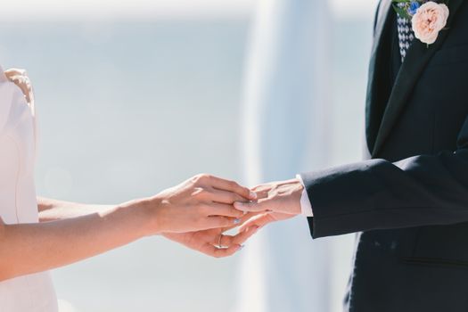 A tender close-up moment of exchanging wedding rings under the bright sun, symbolizing love and commitment.