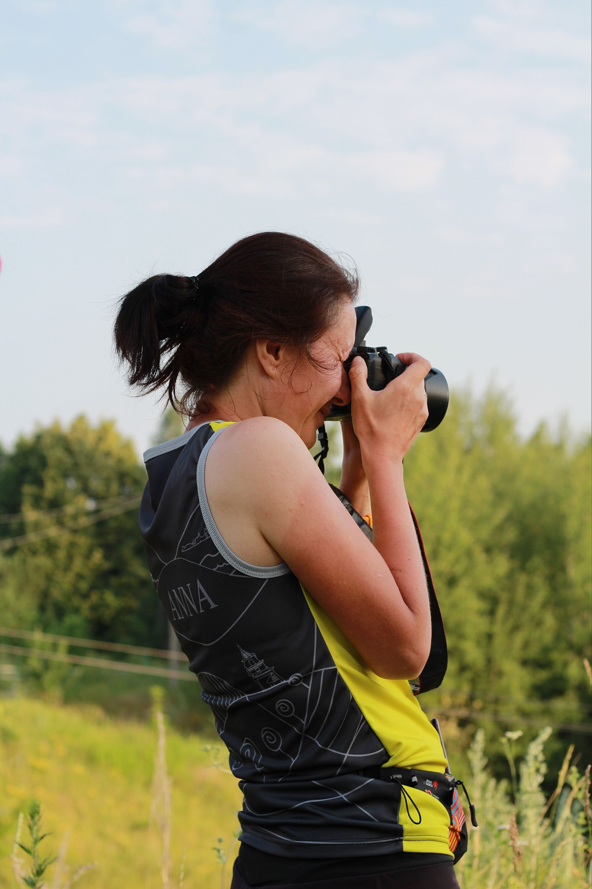 Outdoor image of a woman taking photos with a camera, showcasing summer greenery.