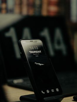 A smartphone on a stand displaying time and date in front of a blurred digital background.